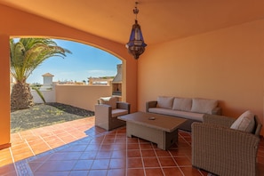 Un patio con un sofá, sillas, una mesa, un farol colgante y vistas a una palmera y edificios.