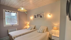 Een slaapkamer met twee bedden, een raam, een plafondventilator, wandlampen en een nachtkastje met een lamp.