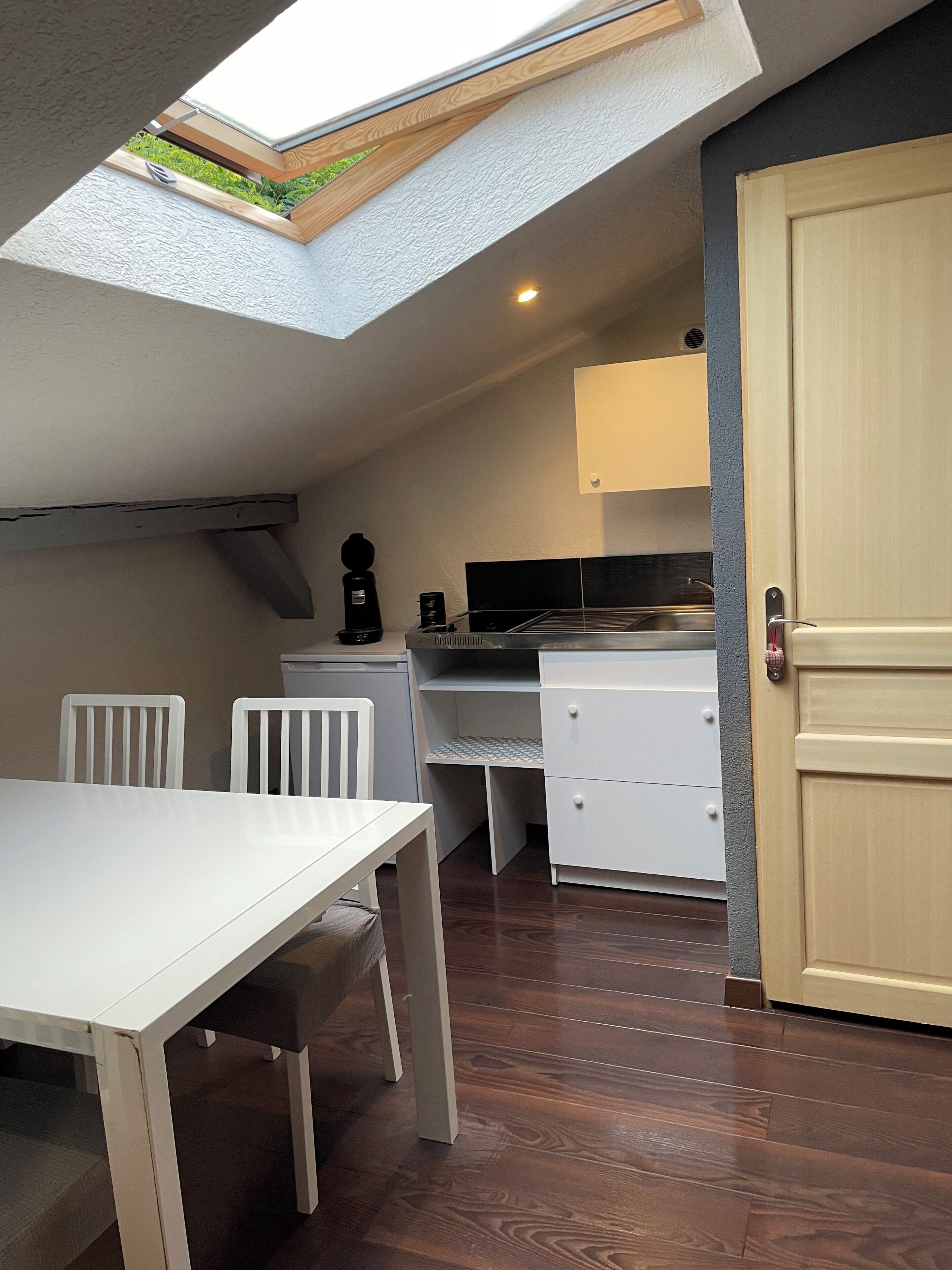 Cocina compacta con tragaluz, armarios blancos, una mesa de comedor con sillas y piso de madera.