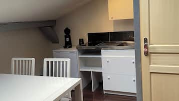 Cocina compacta con tragaluz, armarios blancos, una mesa de comedor con sillas y piso de madera.