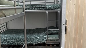 Een slaapkamer met stapelbedden, metalen spijlen, een houten deur en een visgraat vloer.