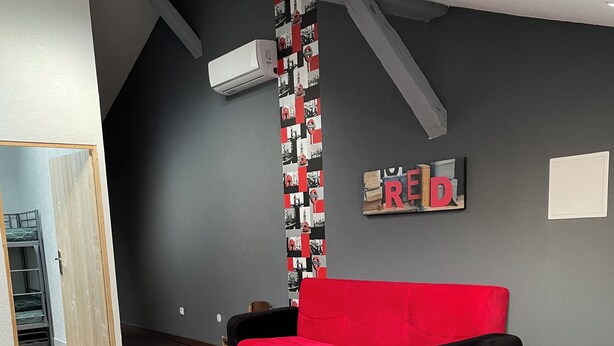 Een moderne woonkamer met een rode bank, een witte tafel en een klein rond tafeltje. De muur is bekleed met behang in zwart-wit en er hangt een rood-wit bordje met de tekst 'REID'.