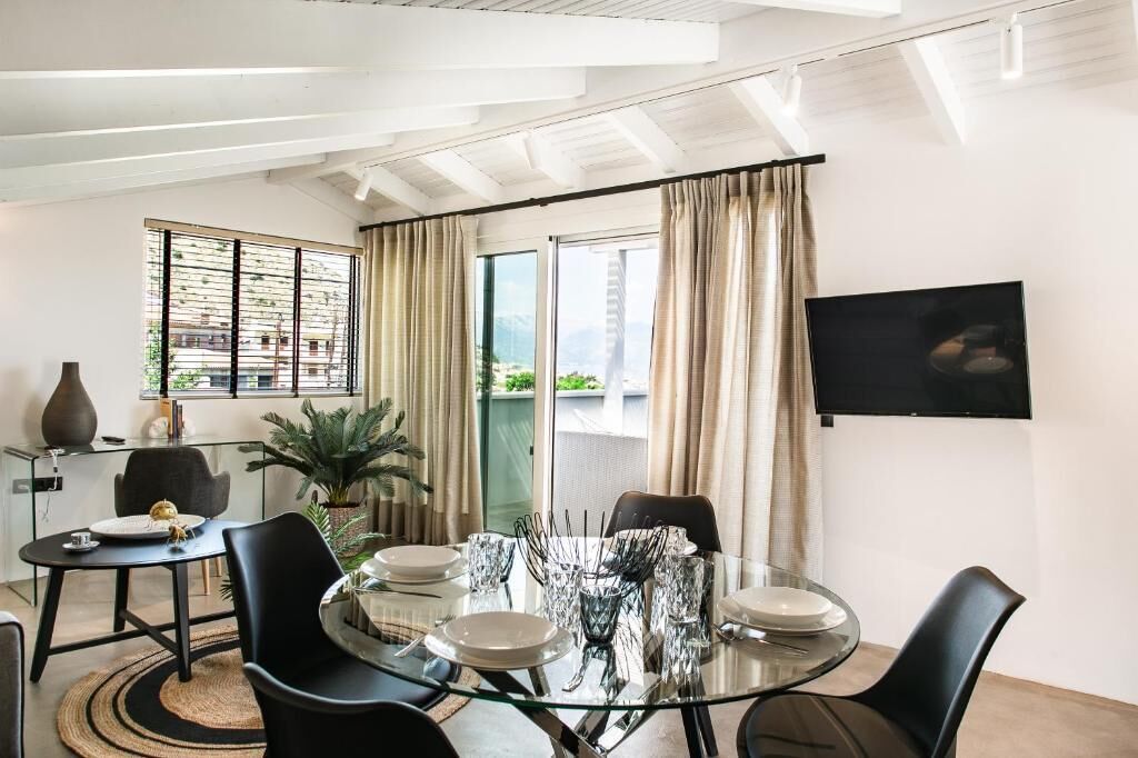 A dining area with a glass table, black chairs, and a view of a cityscape through large windows.