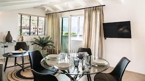 Un comedor con una mesa de vidrio, sillas negras y vistas a un paisaje urbano a través de ventanas amplias.