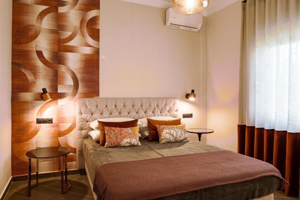 Ein Schlafzimmer mit einer gesteppten Kopfstütze, zwei Nachttischen, einem Bett mit brauner Decke und einer Wand mit geometrischem Muster.