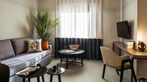 Una sala de estar con sofá, mesa de centro, mesa de comedor con sillas, televisor y un ventanal con cortinas.