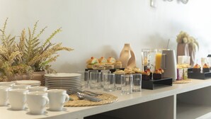 A buffet setup with plates, cups, and glasses on a table, accompanied by decorative plants and a coffee station. - Duna Queen Hotel Conceito (Barreirinhas)