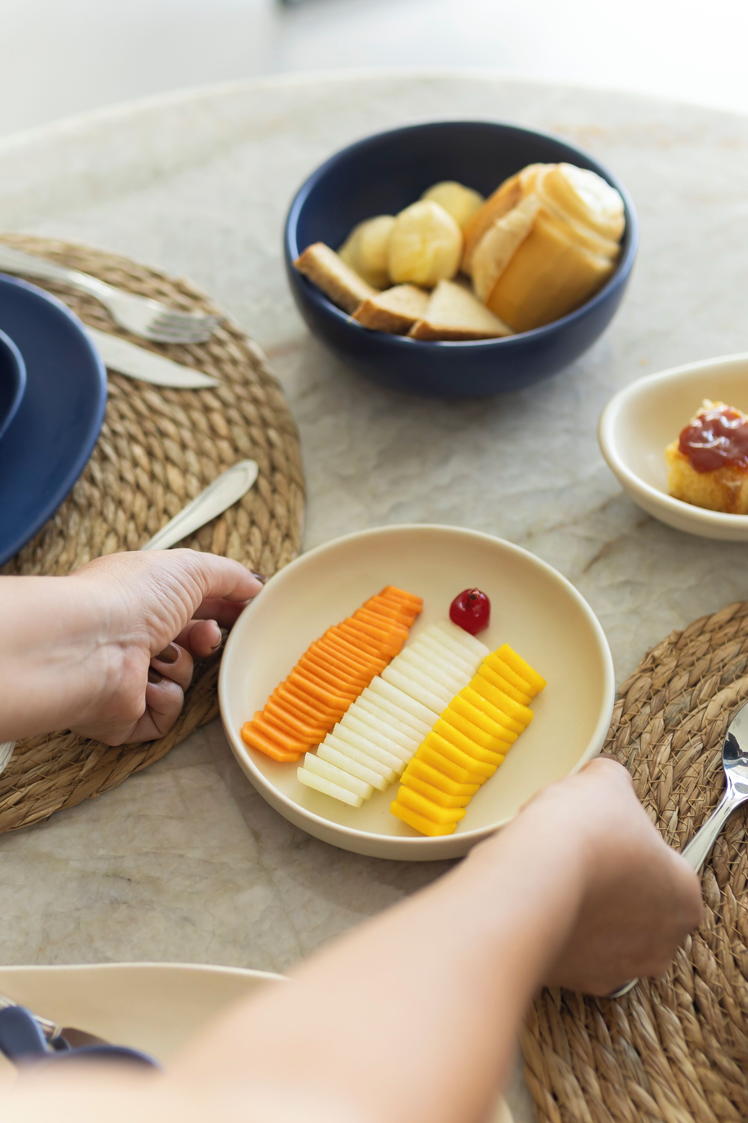 A dining table with plates of food, a bowl of bread, and a small dish with ketchup.