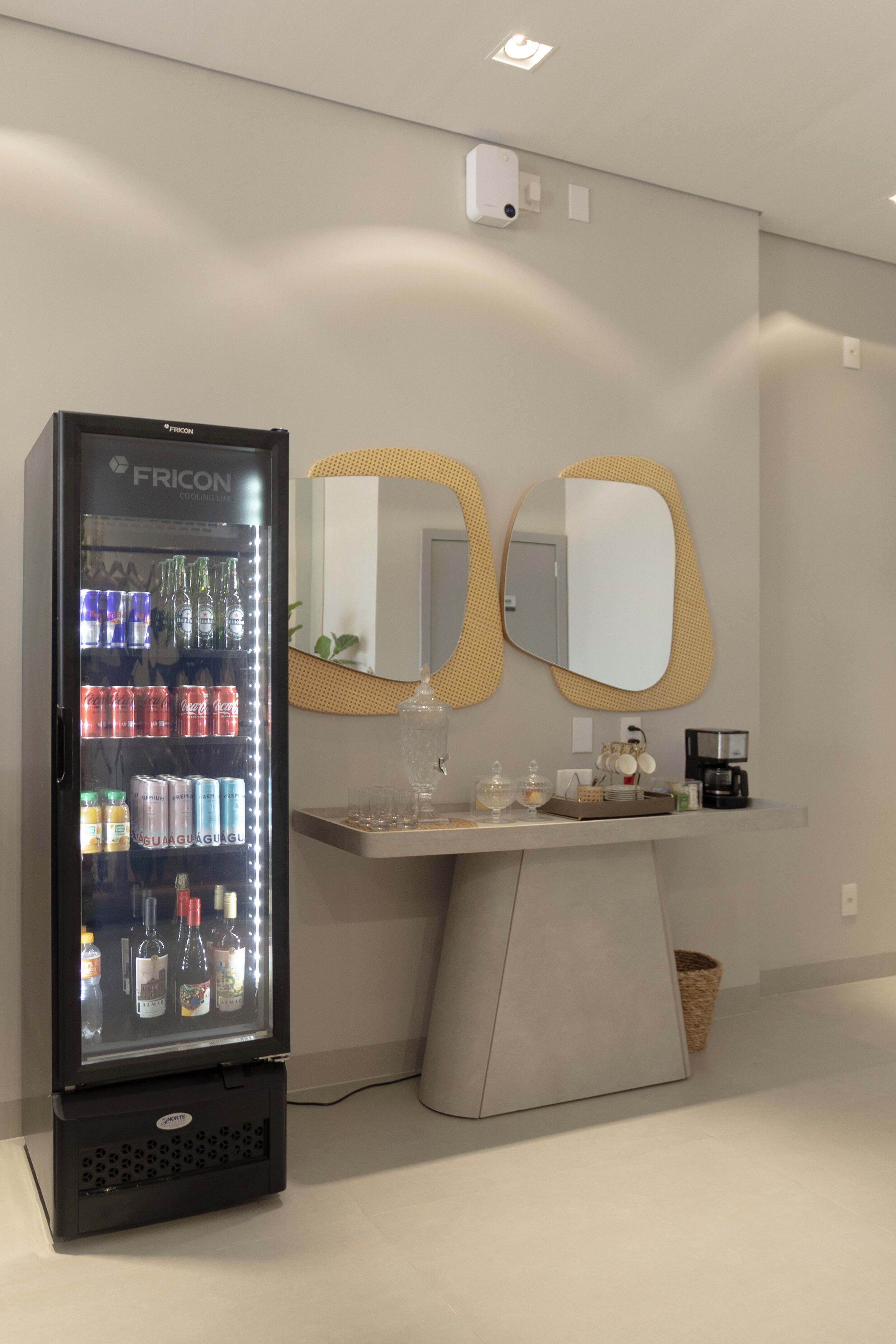 A minibar with a Fricon cooler, a coffee machine, and a small table with glasses and a basket.