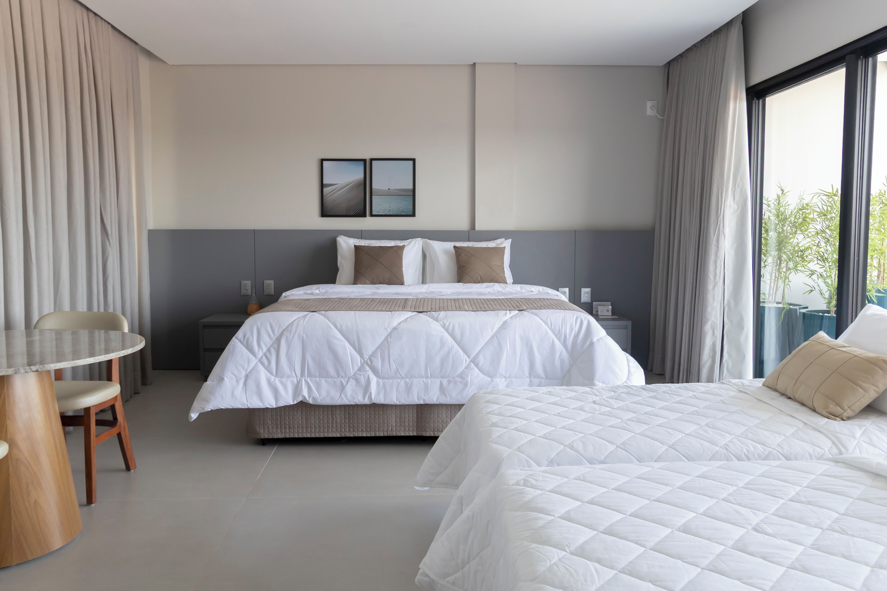 A modern hotel room with a large bed, a dining table, and a view of the outdoors.