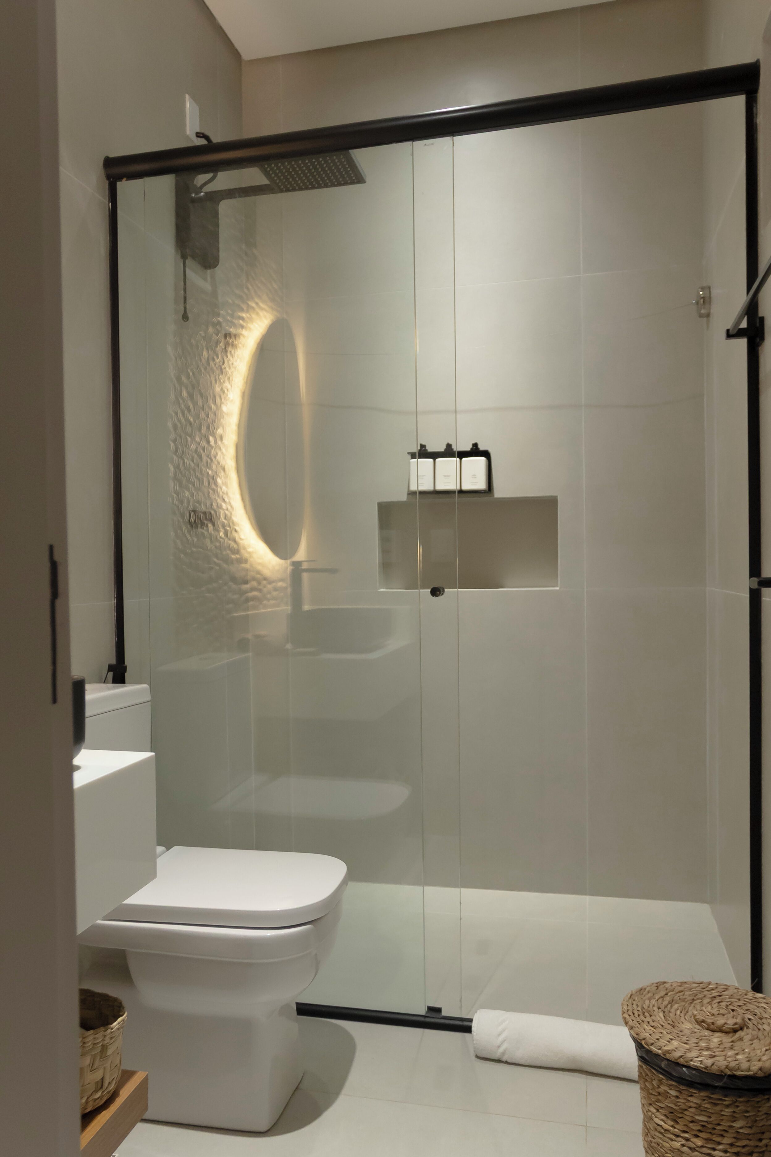 A modern bathroom with a glass-enclosed shower, a white toilet, a sink, and a small wicker basket.