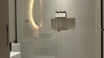 A modern bathroom with a glass-enclosed shower, a white toilet, a sink, and a small wicker basket.