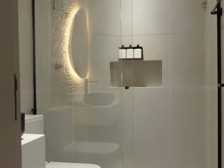 A modern bathroom with a glass-enclosed shower, a white toilet, a sink, and a small wicker basket.