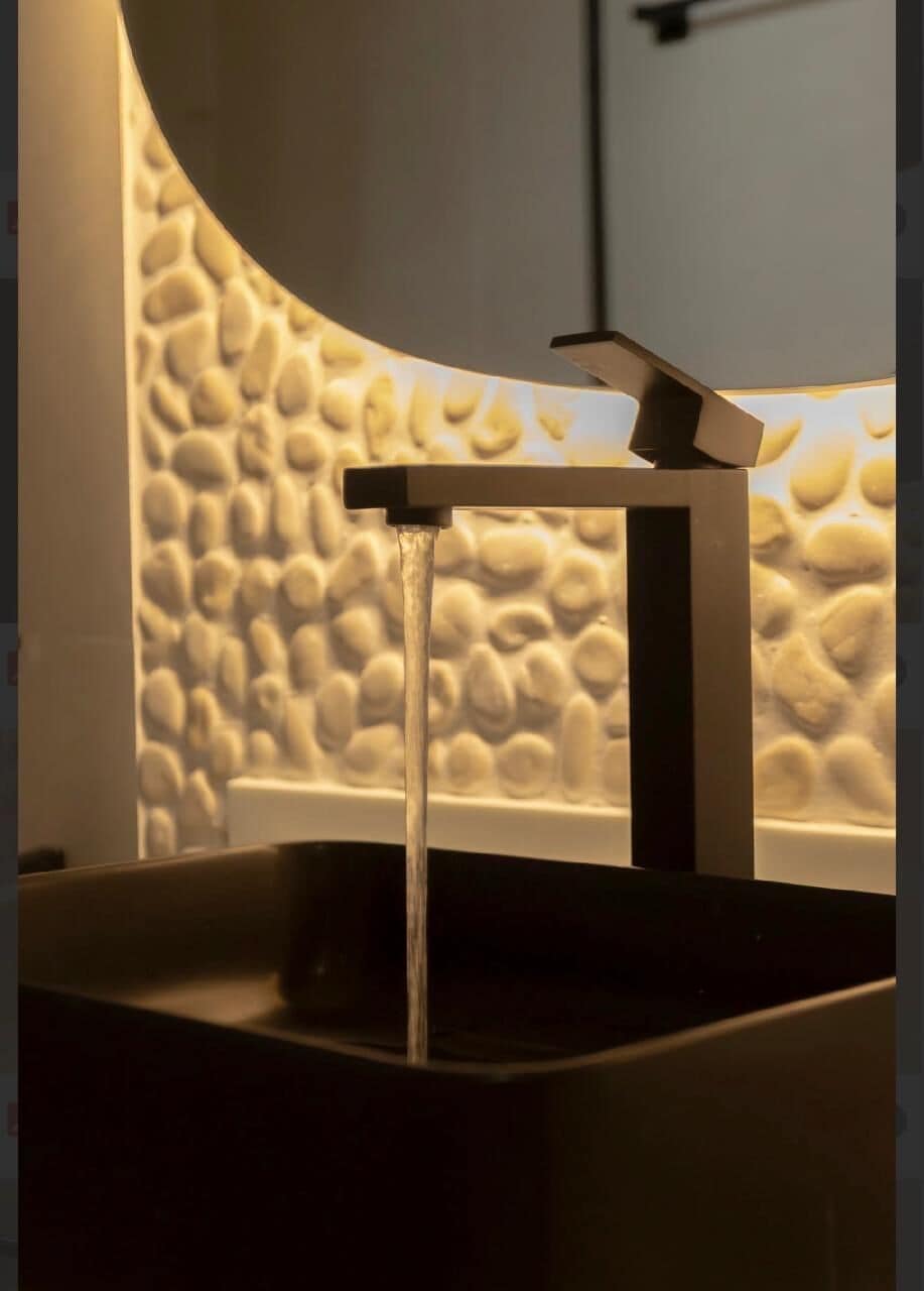 A modern bathroom with a unique pebble wall design, a minimalist faucet, and a sleek, dark countertop.