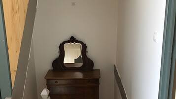 Un escalier étroit avec des marches en bois et une rampe blanche, menant à une pièce où se trouvent une commode en bois et un miroir.