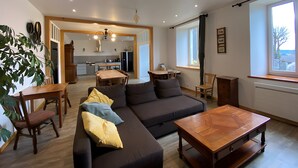 A spacious living area with a sofa, wooden coffee table, and dining table. A kitchen is visible in the background. - Maison 'Lilas Rose' 300m², 12 guests, private garden and barbecue (Le Mas-de-Tence)
