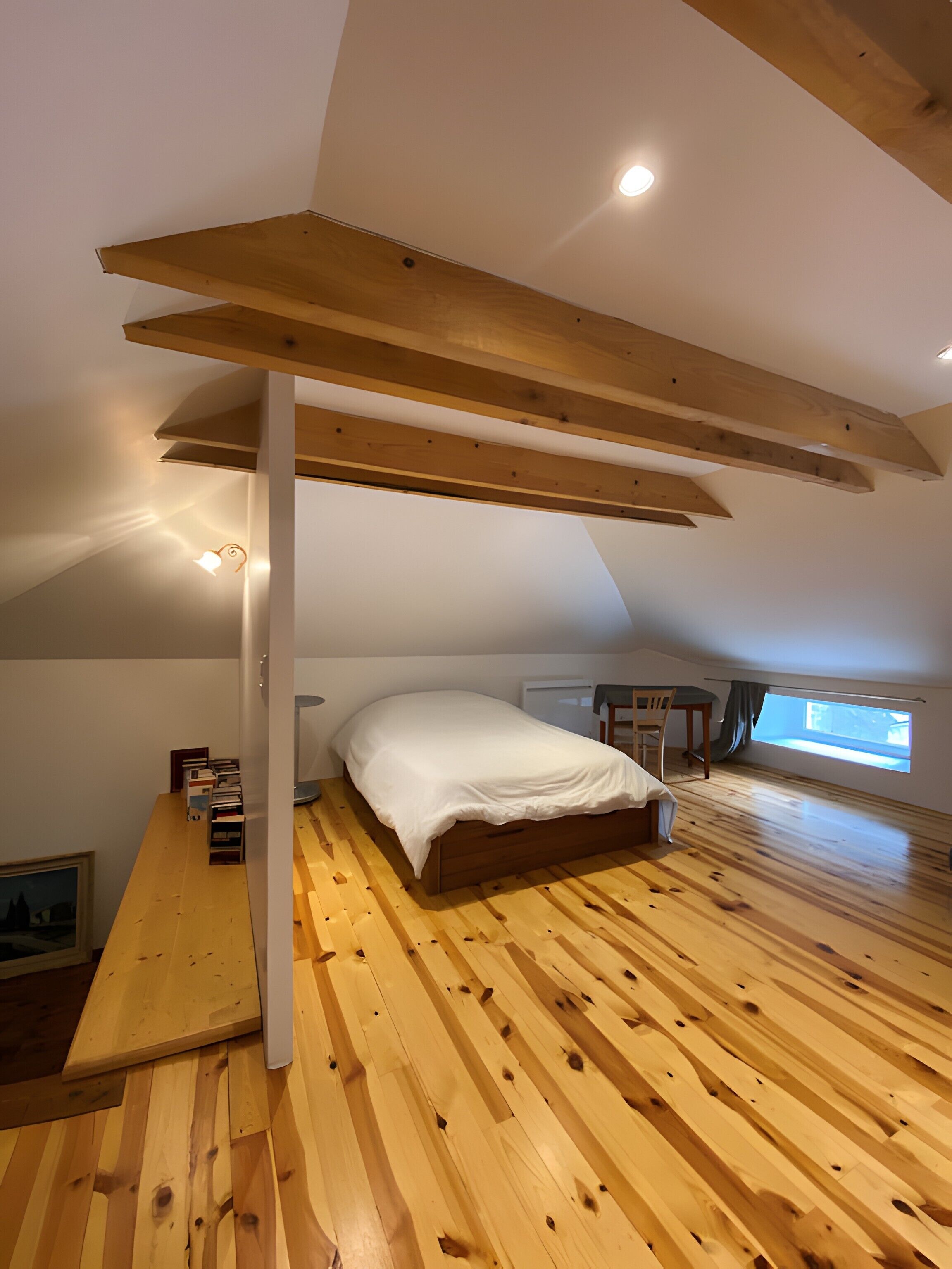 Slaapkamer in een loft met schuine wand, houten balken, een bed, bureau en raam.