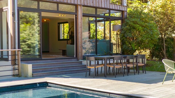 Una casa moderna con piscina, mobiliario exterior y grandes ventanales.