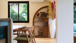 Un comedor con muebles de madera, un jarrón blanco con plantas secas y una ventana con vistas a zonas verdes.