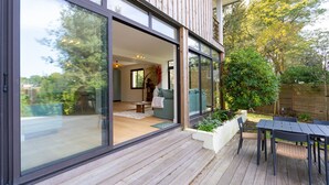 Una casa moderna con amplios ventanales correderos, una terraza de madera y un patio con mesa y sillas.