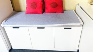 Ein Bett mit grauem Matratze und zwei roten Kissen mit kreisförmigem Muster, ein weißer Nachttisch und eine weiße Kommode mit schwarzen Griffen.