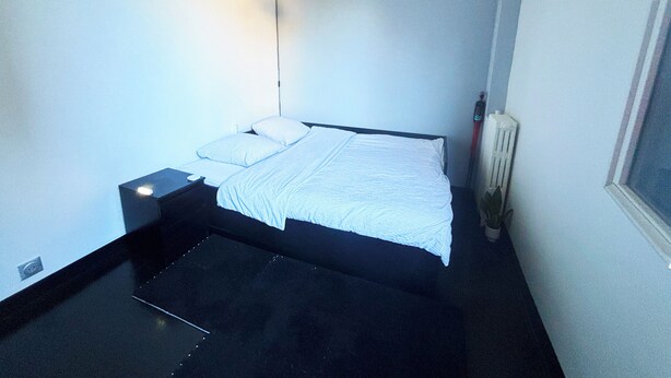 Ein kleines, modernes Schlafzimmer mit einem Einzelbett, einem Nachttisch, einer Pendelleuchte und einer Heizung.