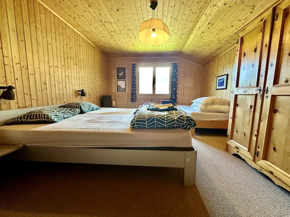 Una habitación con paredes y techo de madera, una cama con ropa de cama estampada, una lámpara de noche y un armario.