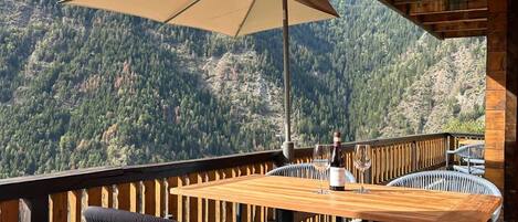A wooden deck with a table and chairs, overlooking a mountainous landscape.