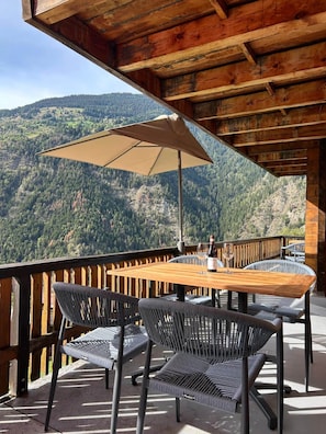Una terraza de madera con mesa y sillas, con vista a un paisaje montañoso.