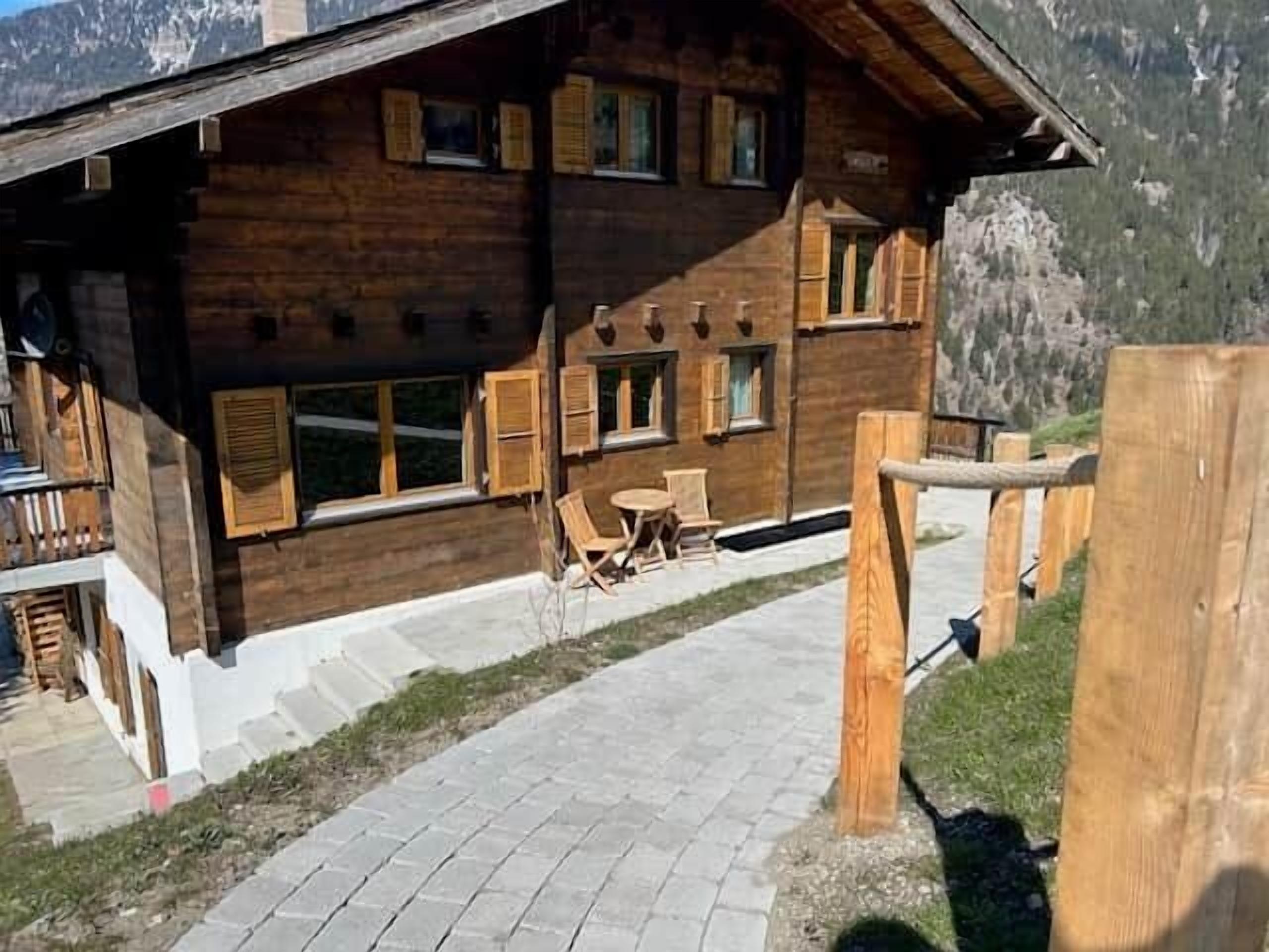 Un bâtiment en bois doté de nombreuses fenêtres et d’une zone pavée avec des chaises.