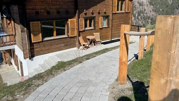 Ein Holzhaus mit vielen Fenstern und einer gepflasterten Fläche mit Stühlen.
