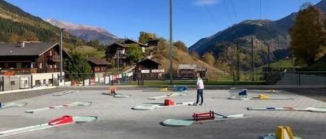 An outdoor ski area with a person standing, surrounded by ski equipment and buildings in the background.