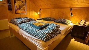 Ein Zimmer mit Holzwänden, zwei Betten, jeweils mit gestreifter Bettwäsche, und Nachttischen mit Lampen.