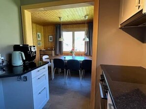 Une cuisine compacte équipée d’une machine à café, d’un coin repas avec des chaises et une table, et d’une fenêtre avec des rideaux.