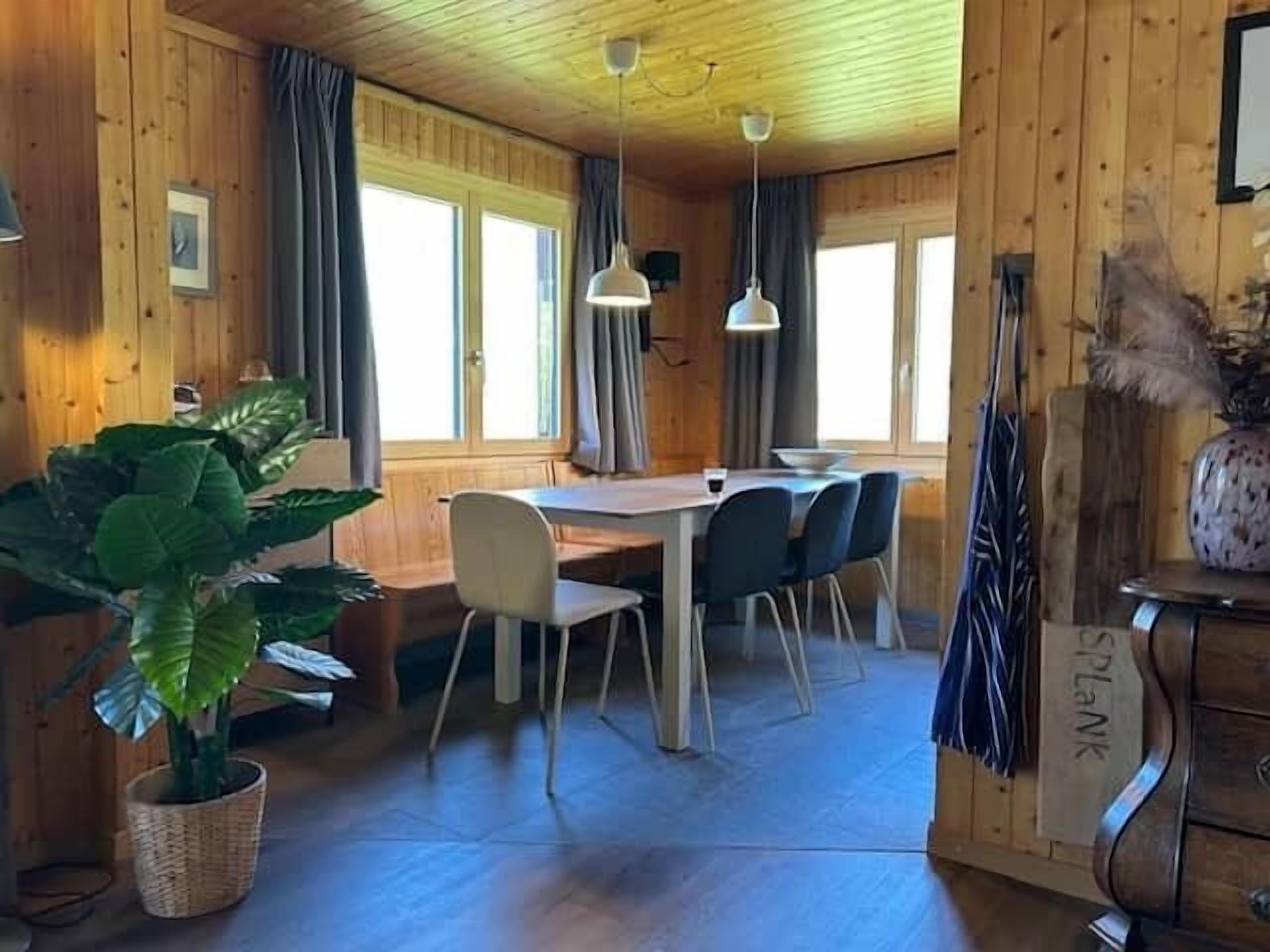 L’intérieur d’un chalet en bois comprend une table à manger, des chaises, une plante en pot et une commode.