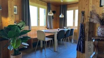 L’intérieur d’un chalet en bois comprend une table à manger, des chaises, une plante en pot et une commode.