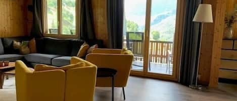 A wooden interior with a sofa, chairs, and a view through a glass door.