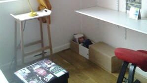 A room with a white desk, a standing lamp, a red chair, wooden shelves with boxes, and a window with curtains. - SINGLE ROOM (Nanterre)