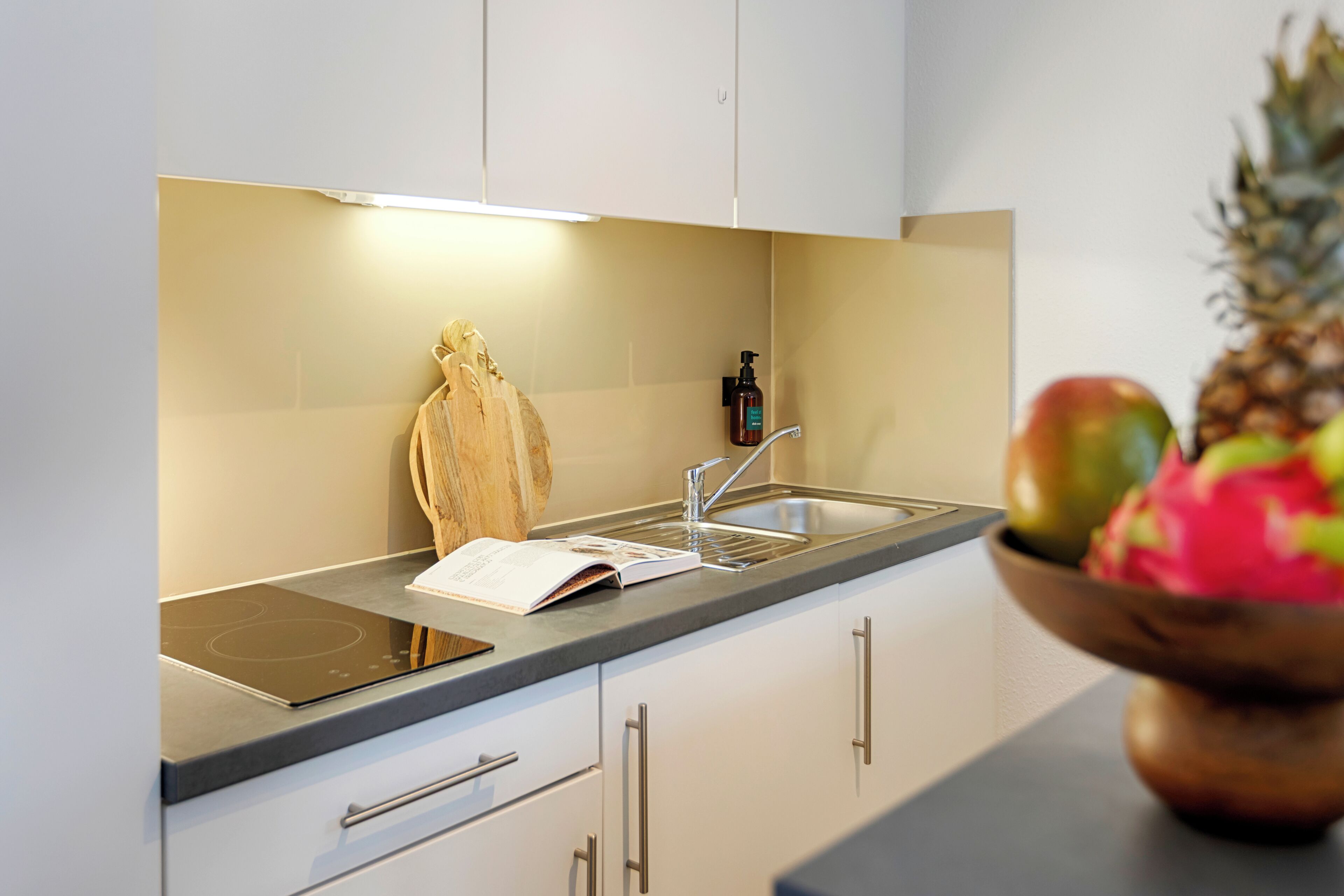 Eine moderne Küche mit eingebautem Herd, Schneidebrett aus Holz, Spüle und einer Schüssel mit Obst.
