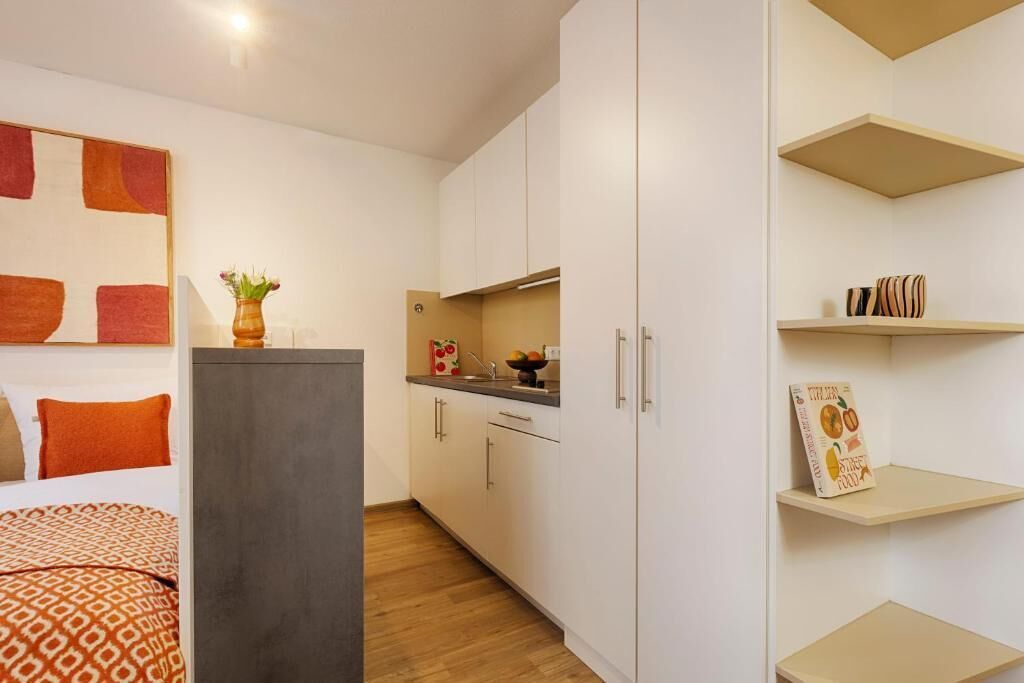 Una habitación de hotel pequeña con cama, kitchenette y baño.
