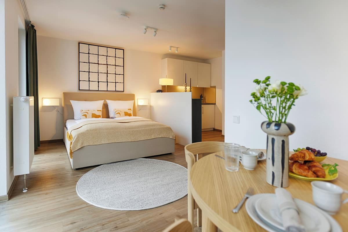 A hotel room with a bed, bedside table, breakfast table, and a view of the kitchen.