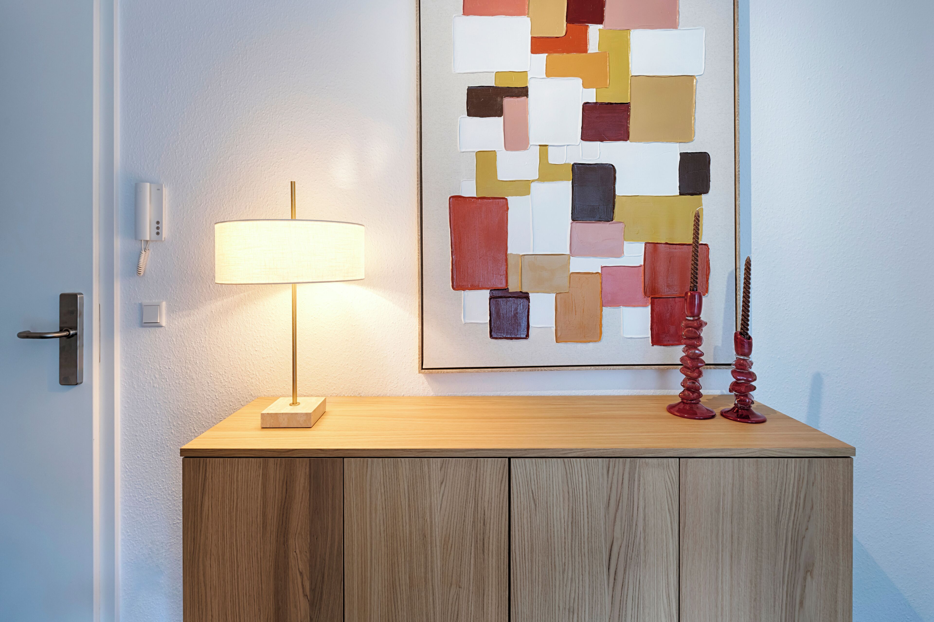 A wooden cabinet with a lamp and a colorful abstract painting above it.