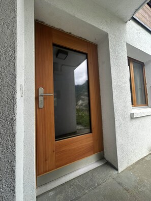Eine Holztür mit Fensterglas, einem Metallgriff und einem kleinen Fenster zur rechten Seite.