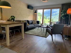 Ein modernes Wohnzimmer mit Essbereich, einer Couch, einem Couchtisch und Blick ins Freie.
