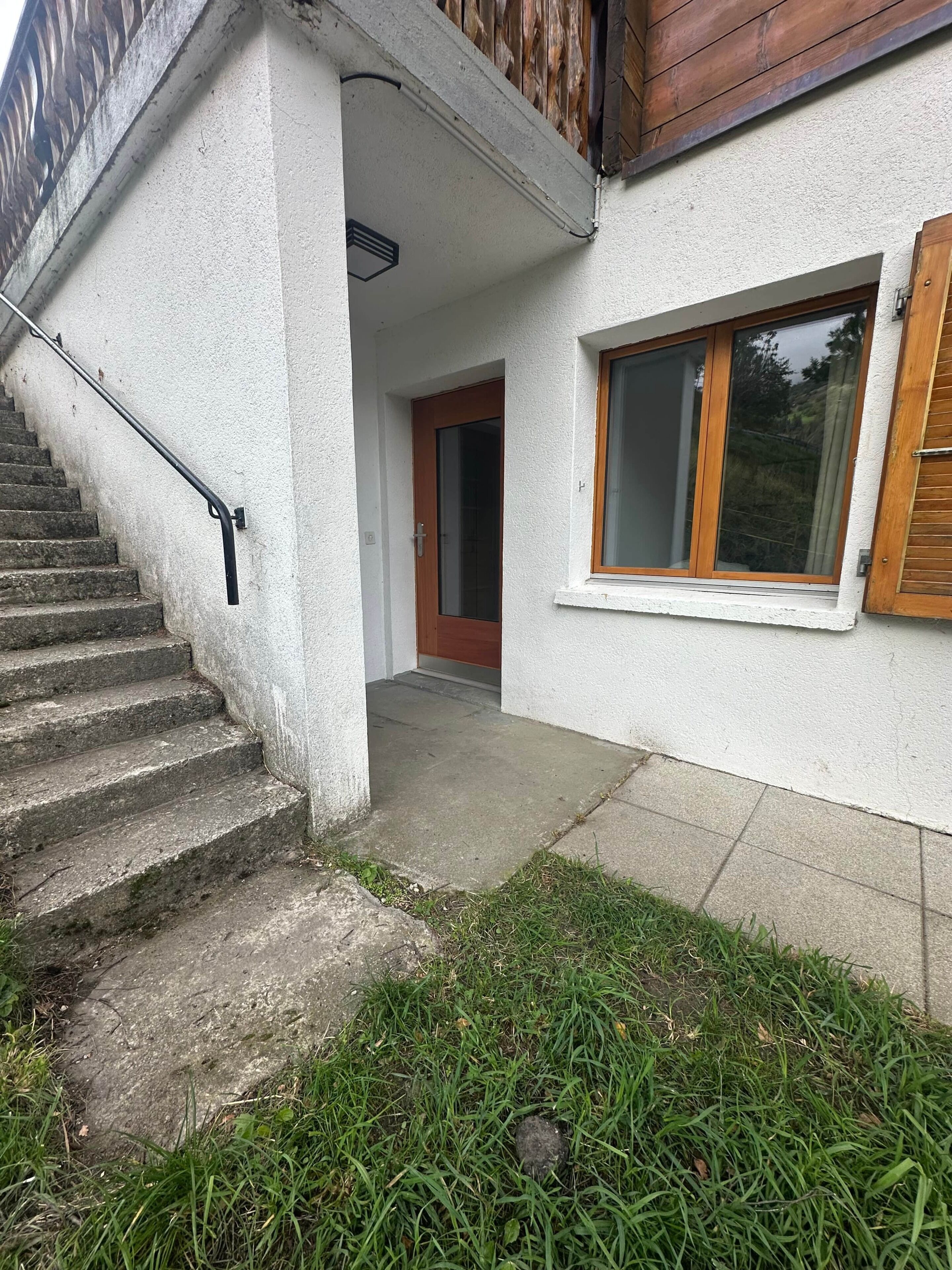 A residential building with a concrete staircase, a wooden door, and a window with wooden shutters.