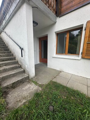 Ein Wohngebäude mit einer Betontreppe, einer Holztür und einem Fenster mit Holzjalousien.