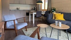 A modern living room with a sofa, chairs, and a coffee table. There is a kitchen area with cabinets and a dining table.