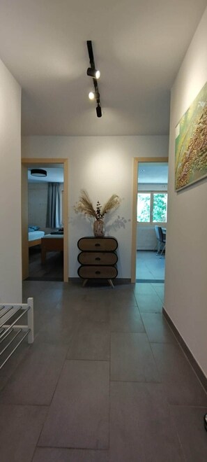 A hallway with a ceiling light, a vase with dried plants, and a painting on the wall. - Chalet Mallum – Lower Apartment (Grengiols)