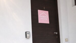 Eine dunkle Holztür mit einem rosa Schild, auf dem 'EMILIA'S HOUSE' und 'CONIO SEE' steht.