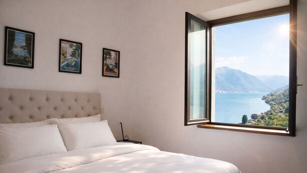 Ein Schlafzimmer mit einem Bett, einem Nachttisch und einem Fenster mit Blick auf einen See und Berge.